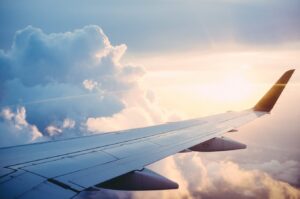 View from an airplane window showing the wing extending over a thick layer of white clouds during a golden sunset