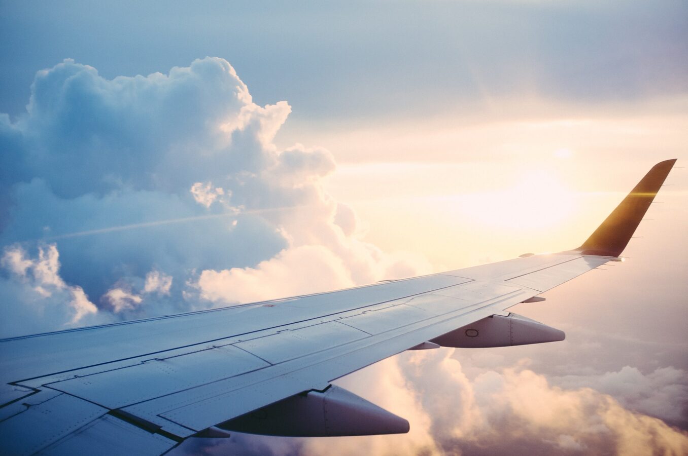 View from an airplane window showing the wing extending over a thick layer of white clouds during a golden sunset