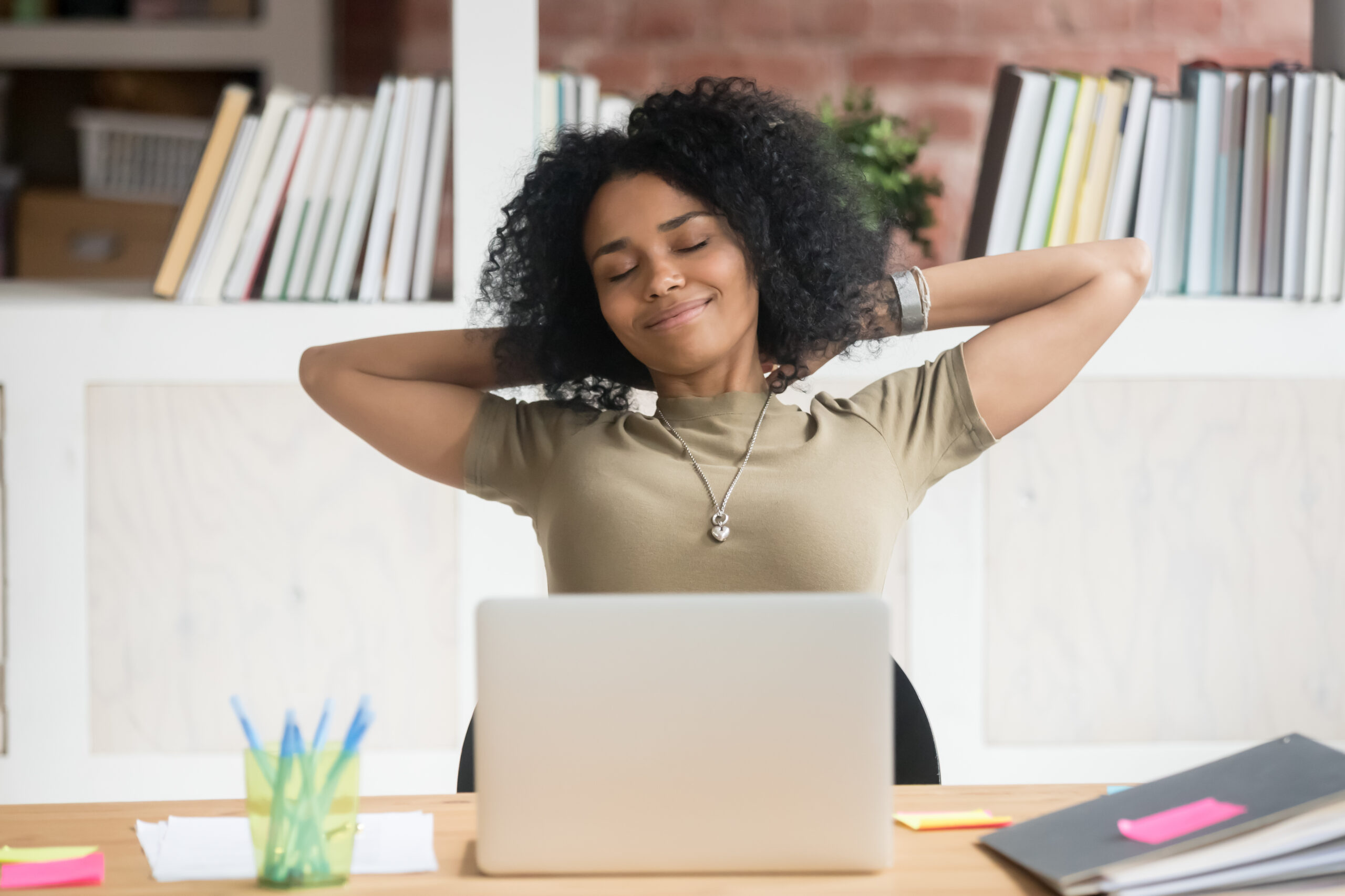 Relaxed woman in front of laptop with hands behind head.