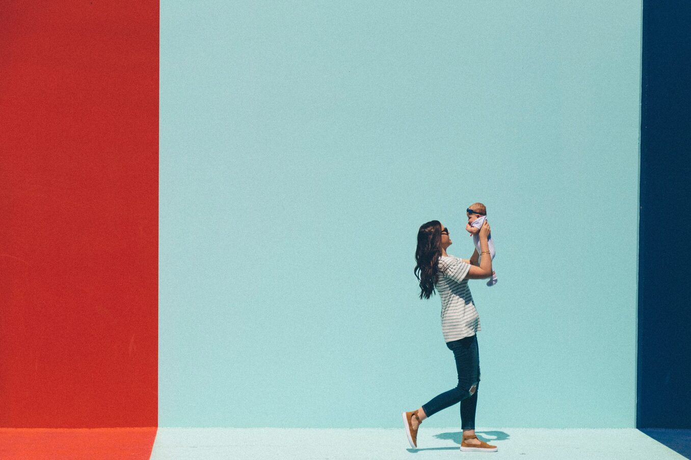 A woman walks with her baby in front of a bright mural