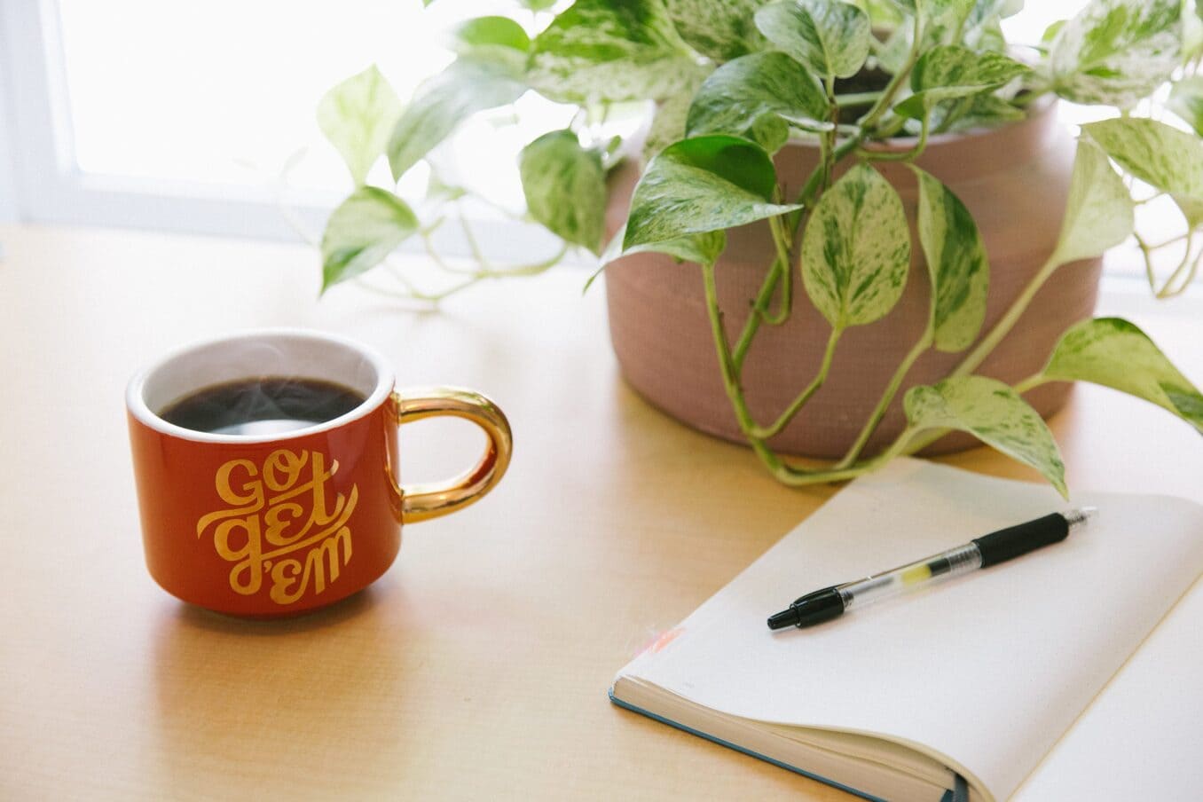 Mug reading "Go Get 'Em" sits next to an open journal with a pen.