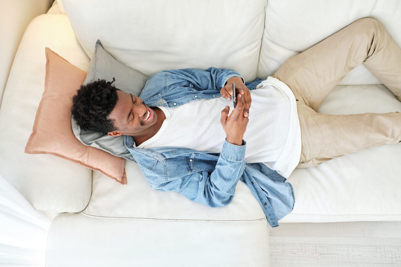 Man lying down on couch, looking at his phone and laughing.