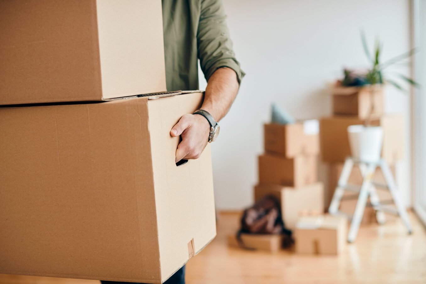 Close up of a man carrying a stack of boxes. Another pile of boxes in the background