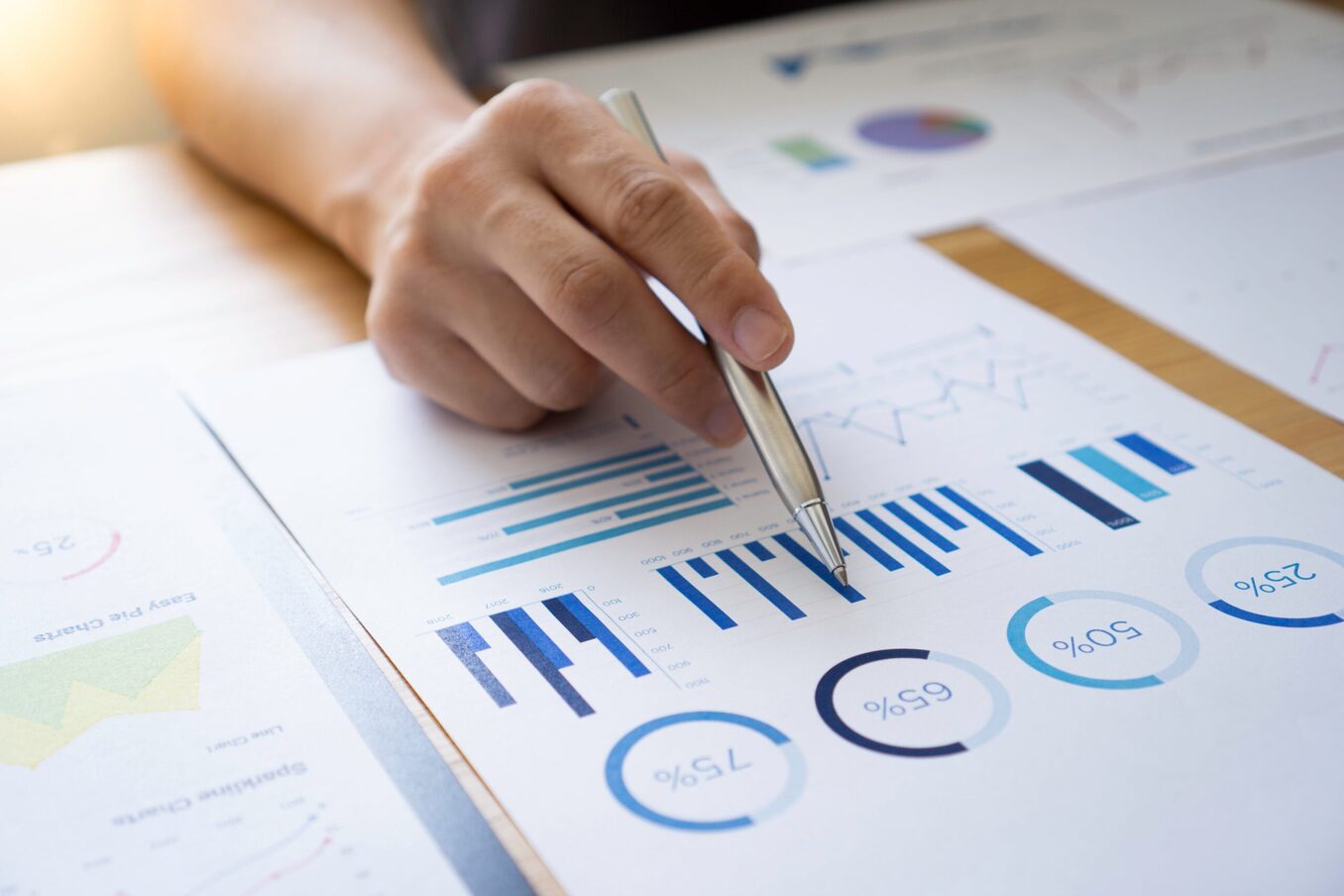 A person reviewing bar and pie charts on paper in front