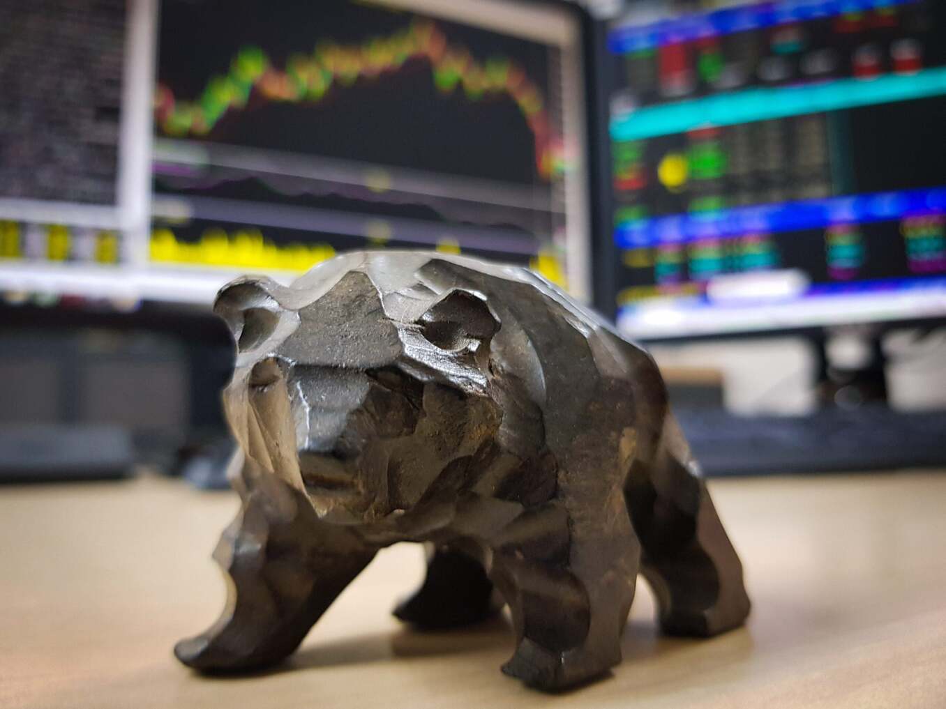 Bear statue sitting on desk. Monitors in the background