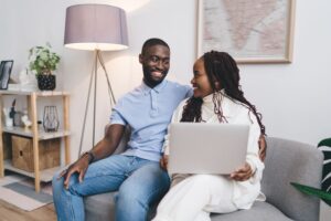 A smiling young couple sitting on a sofa and using a laptop together at home.