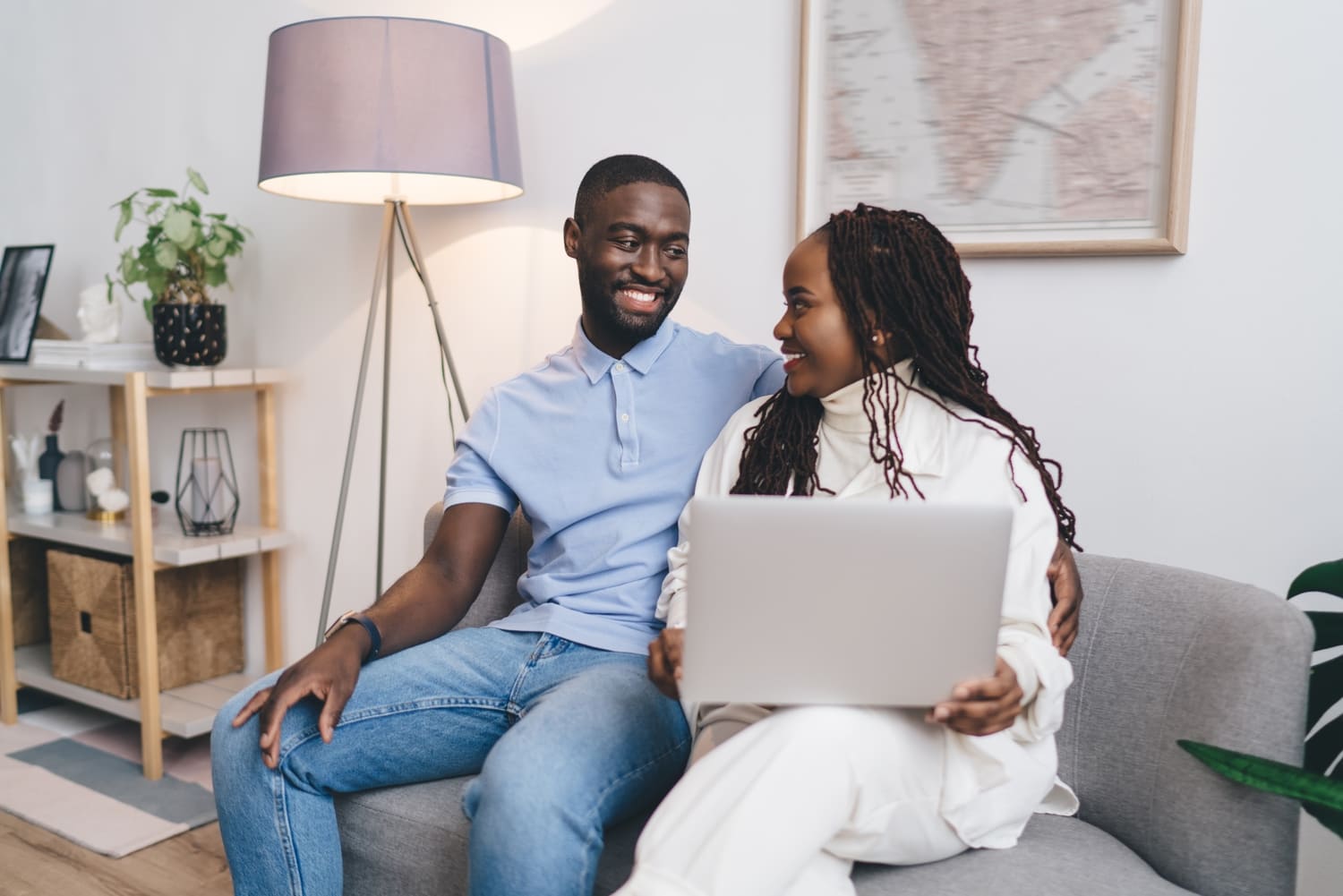 A smiling young couple sitting on a sofa and using a laptop together at home.