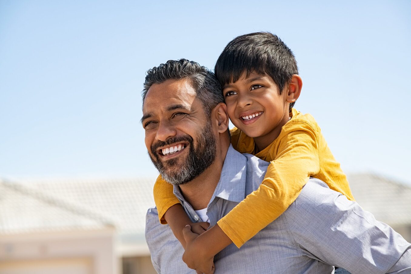A smiling father and son sharing a piggyback ride outdoors.