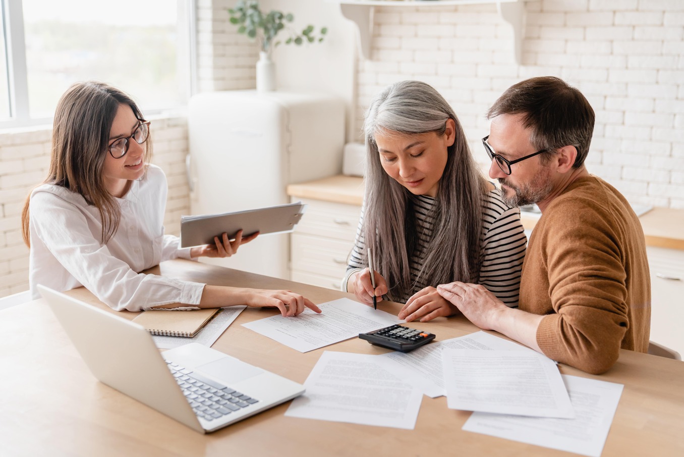 A professional advisor assisting a couple as they sign important paperwork at a desk.