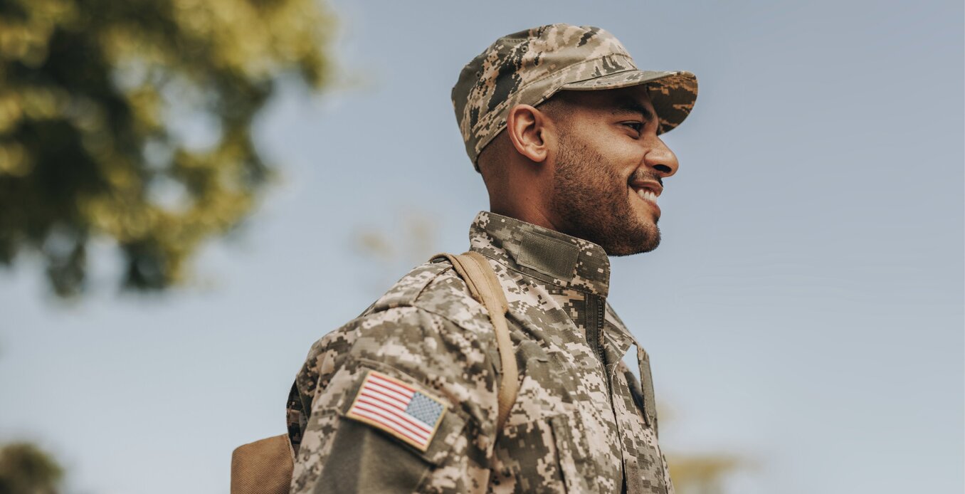 Happy young soldier smiling cheerfully while standing outside his home. Patriotic American serviceman coming back home after serving his country in the military.