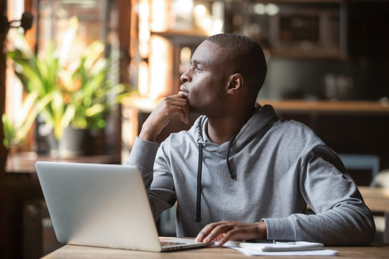 Thoughtful African American businessman lost in thoughts search for inspiration sit at cafe table using laptop