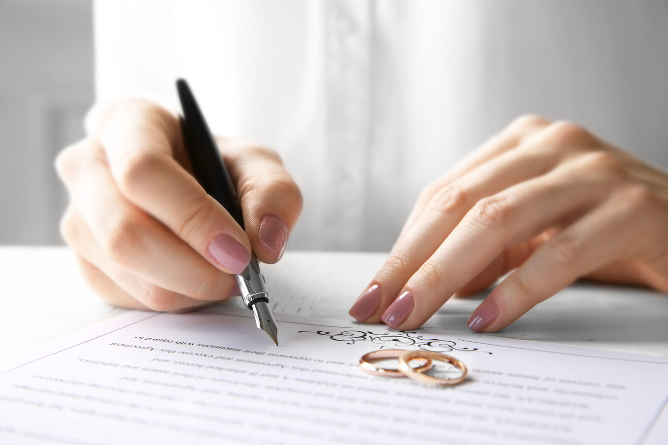 Close-up of a person signing a marriage certificate with wedding rings nearby