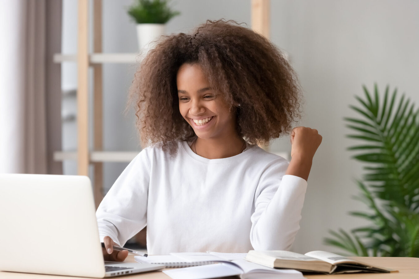 A happy young student celebrating while looking at her laptop