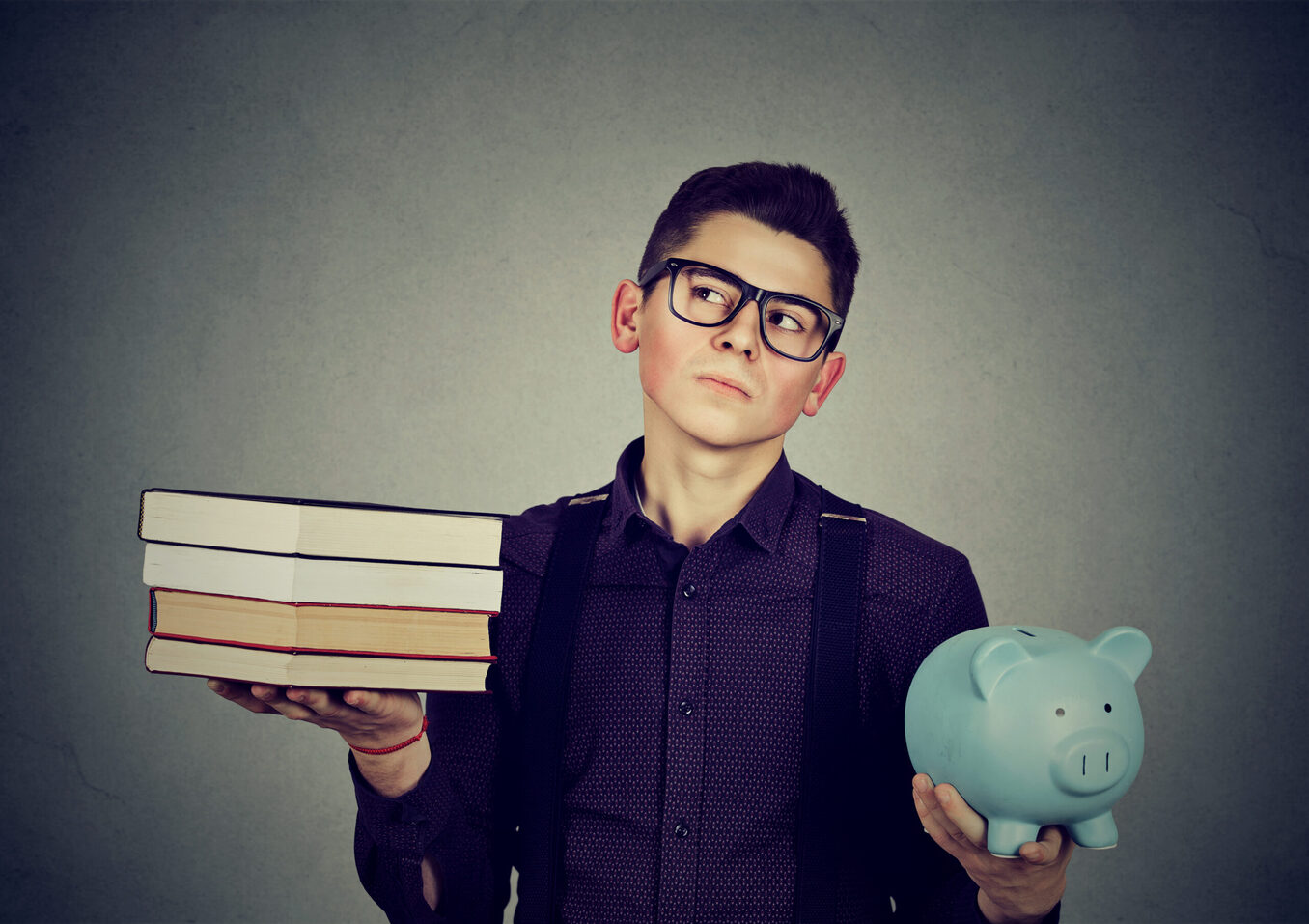Young man with stack pile of books and piggy bank full of debt rethinking future career path