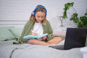 Teenage girl doing homework on the bed.