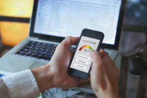 picture of a man's hands holding a smartphone with credit score displayed on the screen with a laptop in the background