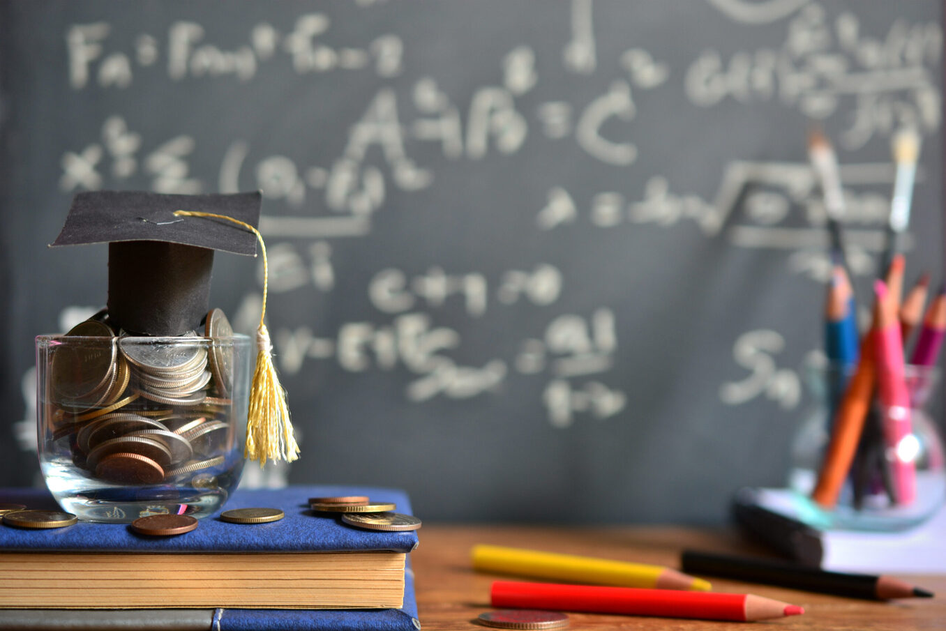 Scholarship concept. Coins, dollar banknotes and graduation cap on wooden table