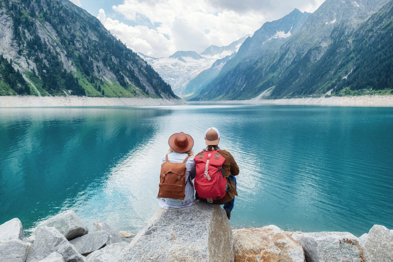 Couple sitting at the edge of a rock and looking into the horizon of a lake with high snowy mountains in front