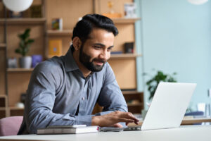 Smiling Indian business man working on laptop at home office.