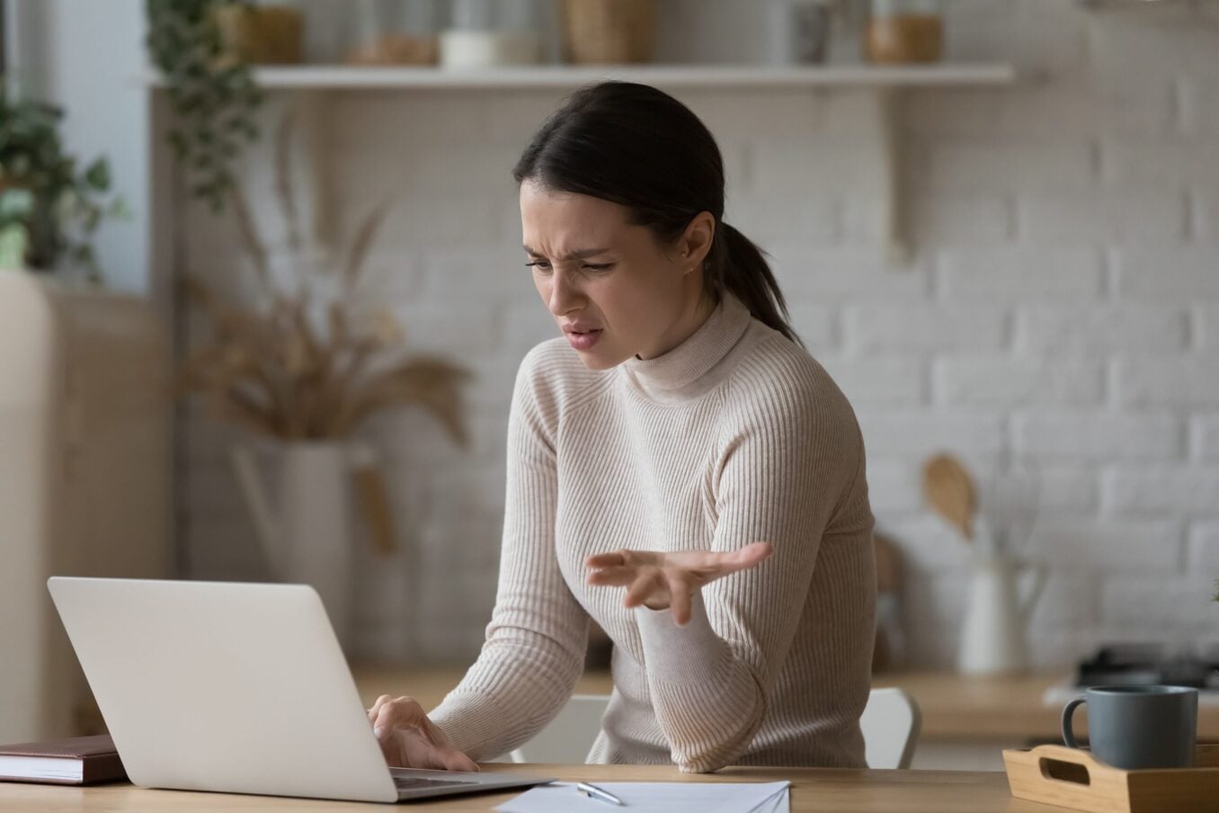 Confused woman sitting at table staring at laptop screen