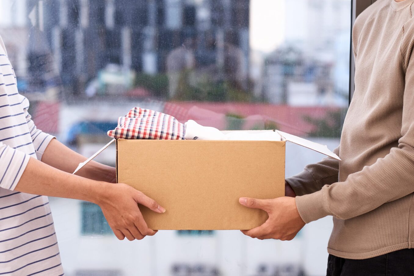 Woman handing box to man. Cityscape in the background