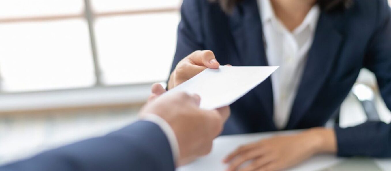 Close-up of a person handing a white envelope to a professional in a suit.