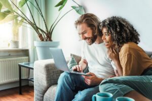 Multiracial young couple watching computer laptop sitting on the sofa