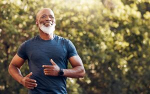 A smiling senior man jogging outdoors in a park.