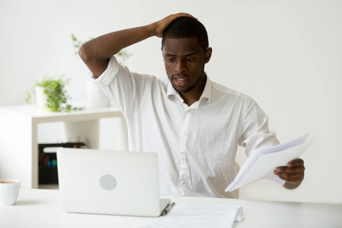 Confused African-American businessman having problem with documents looking at laptop