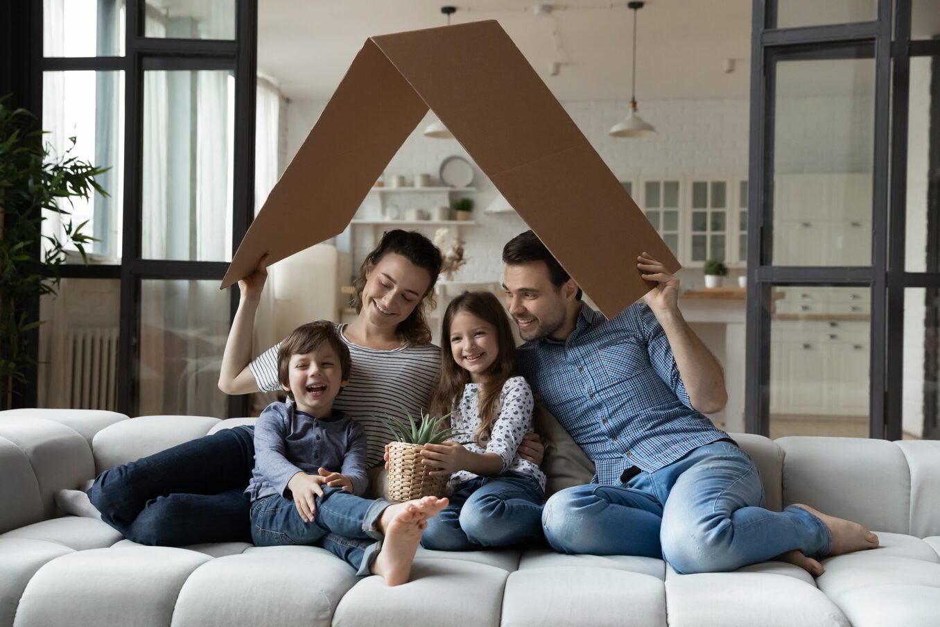 Happy sibling kids and parents holding carton toy roof above