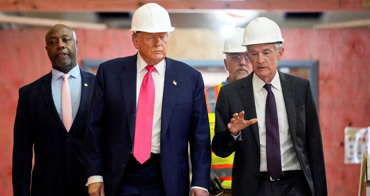 Donald Trump and Jerome Powell wearing white hard hats while walking through a construction site and engaging in conversation.