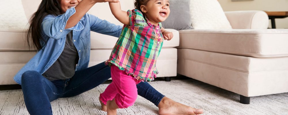 Mother At Home Encouraging Baby Daughter To Take First Steps Mother At Home Encouraging Baby Daughter To Take First Steps