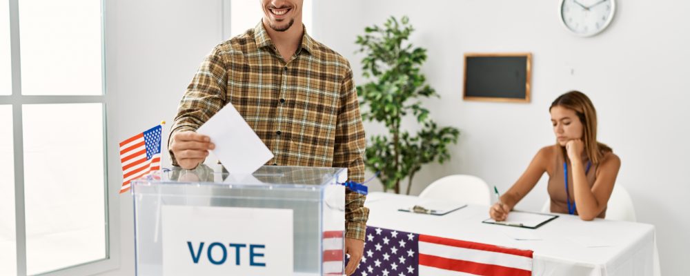 Young,American,Voter,Man,Putting,Vote,In,Ballot,Box,At