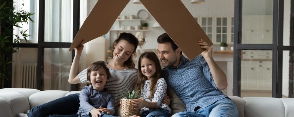 Happy,Sibling,Kids,And,Parents,Holding,Carton,Toy,Roof,Above