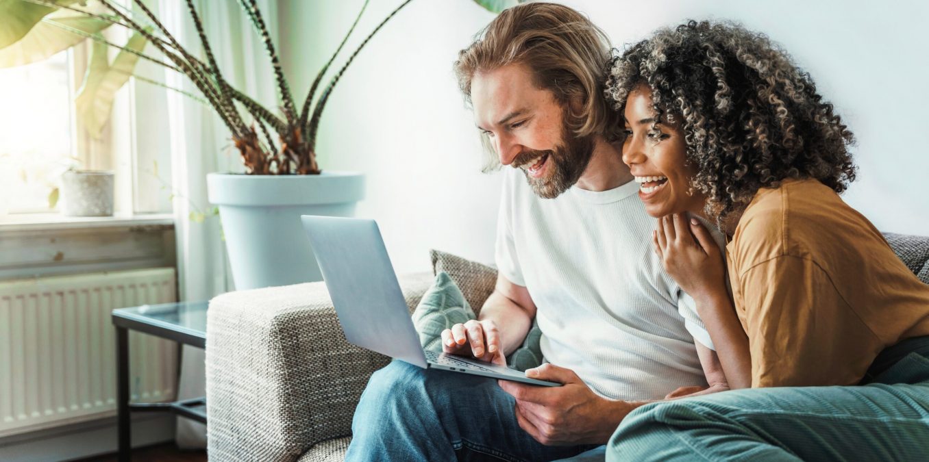 Multiracial,Young,Couple,Watching,Computer,Laptop,Sitting,On,The,Sofa