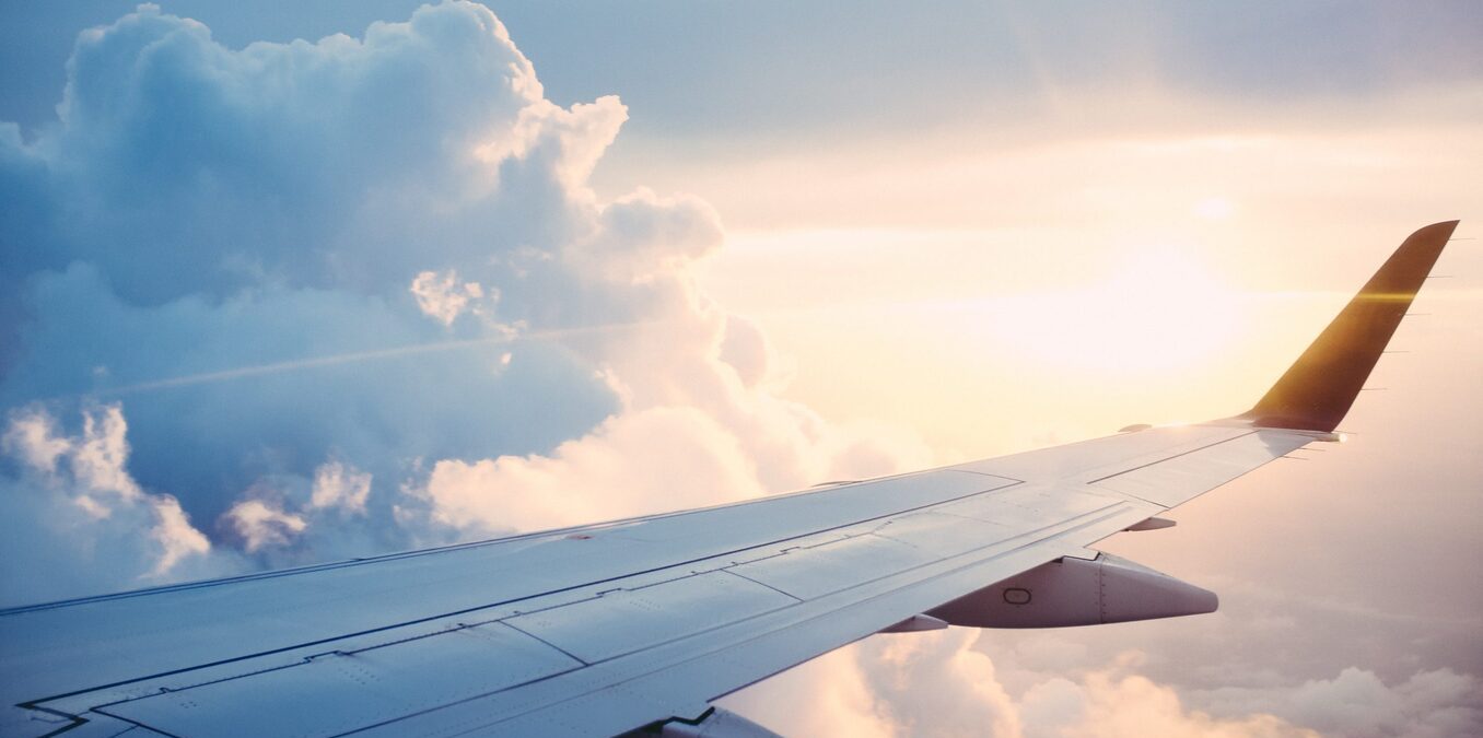 View from an airplane window showing the wing extending over a thick layer of white clouds during a golden sunset
