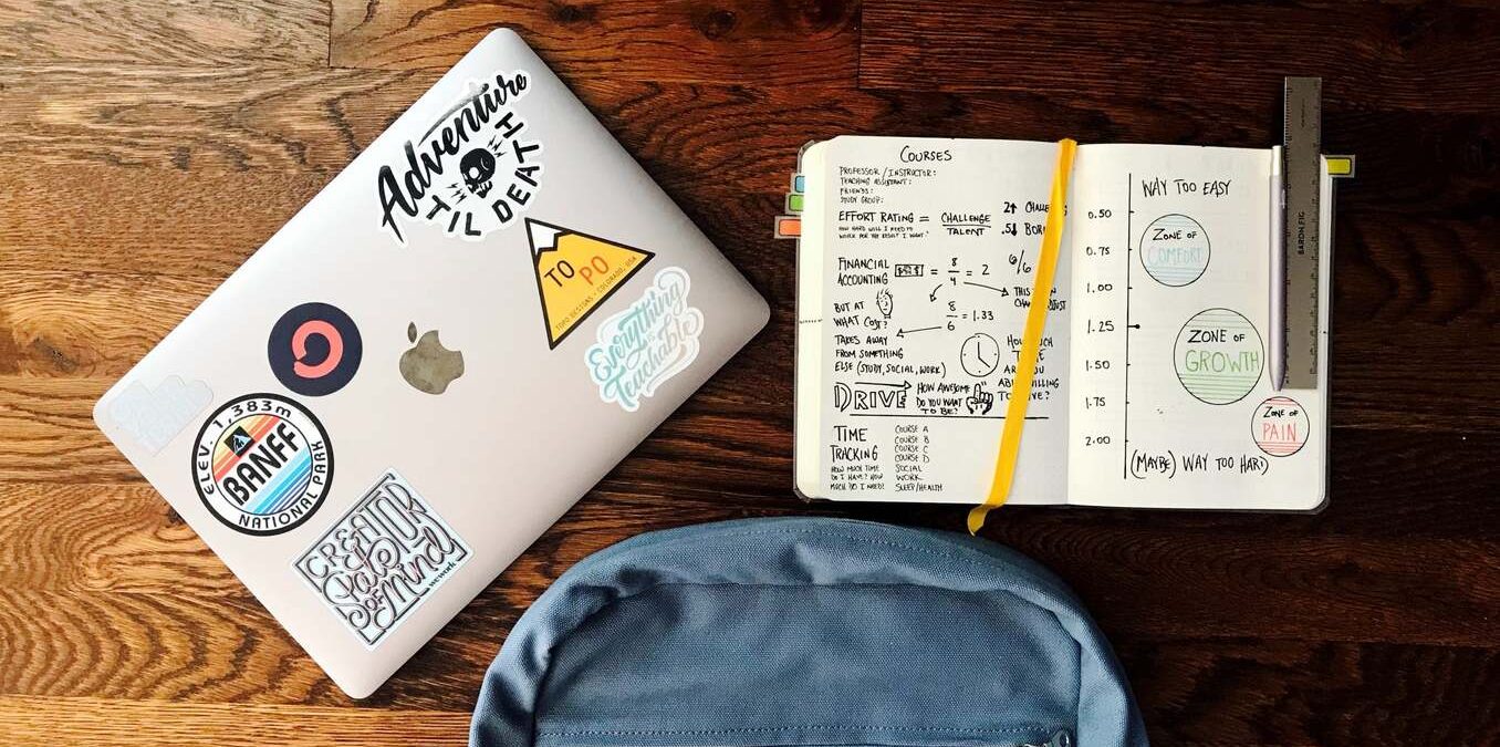 Backpack and laptop sit on a wood table.