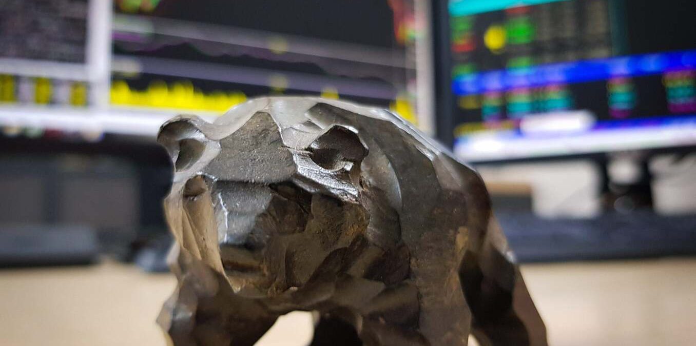 Bear statue sitting on desk. Monitors in the background