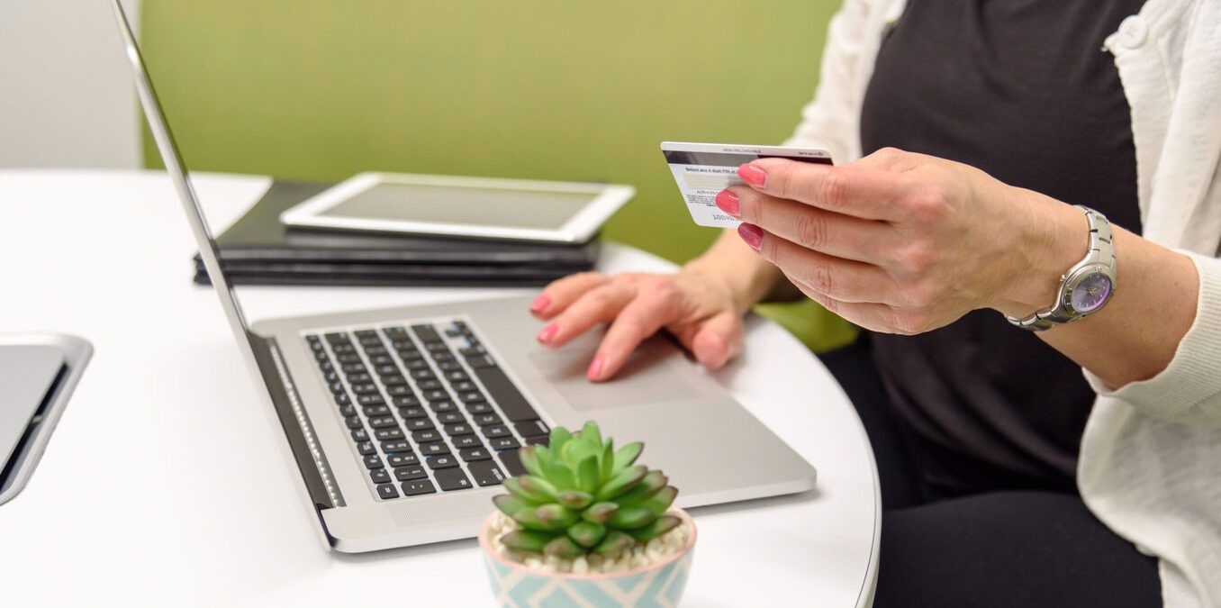 Closeup of a woman holding a credit card at table with laptop computer