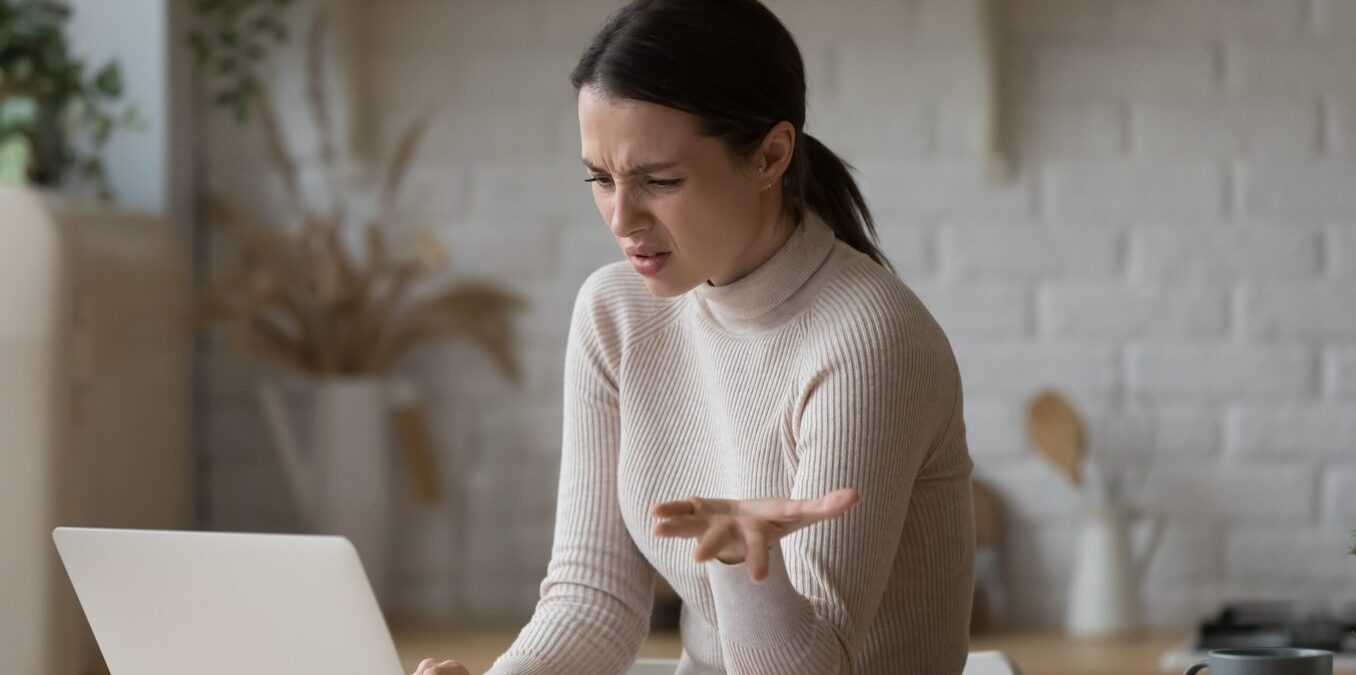 Confused woman sitting at table staring at laptop screen