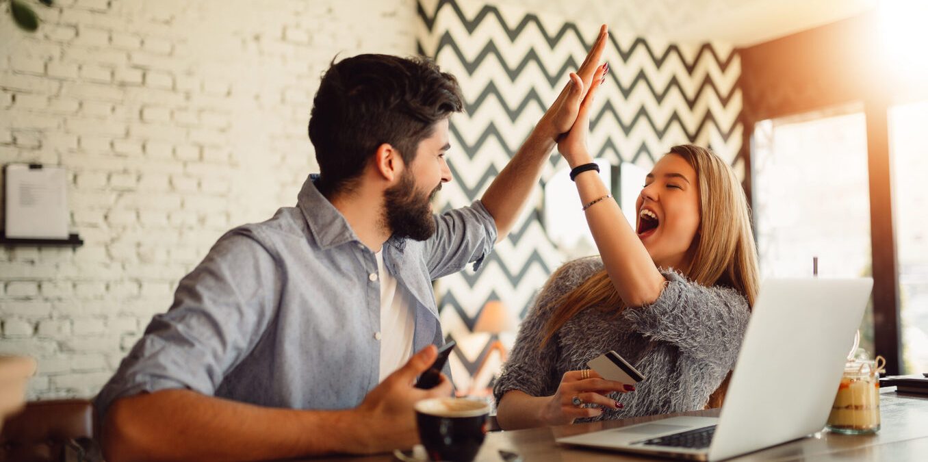 Portrait of an excited young couple giving high five while shopping online.