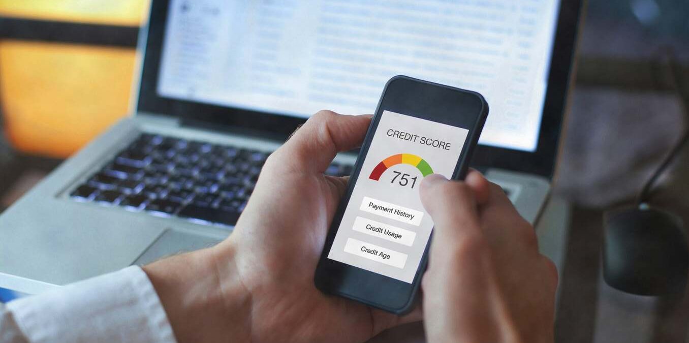 Picture of a man's hands holding a smartphone with credit score displayed on the screen with a laptop in the background