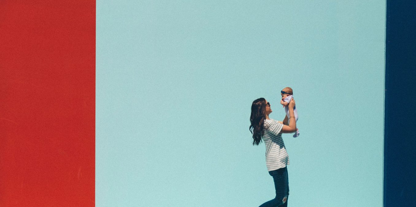 A woman walks with her baby in front of a bright mural.