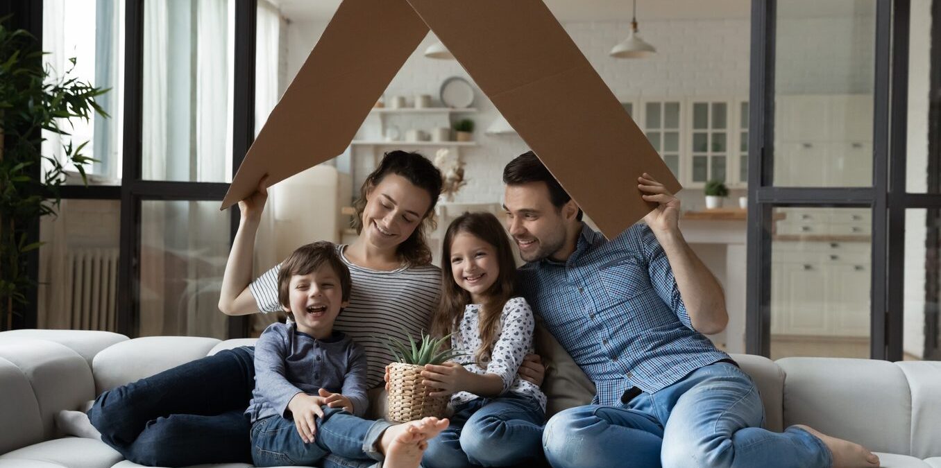 Happy sibling kids and parents holding carton toy roof above