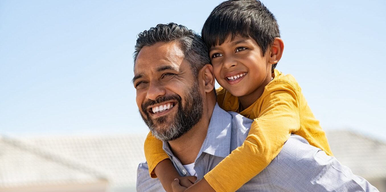 A smiling father and son sharing a piggyback ride outdoors.
