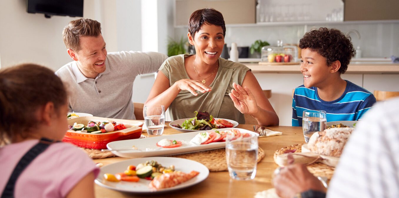 Father Serving As Multi-Generation Mixed Race Family Eat Meal Around Table At Home Together