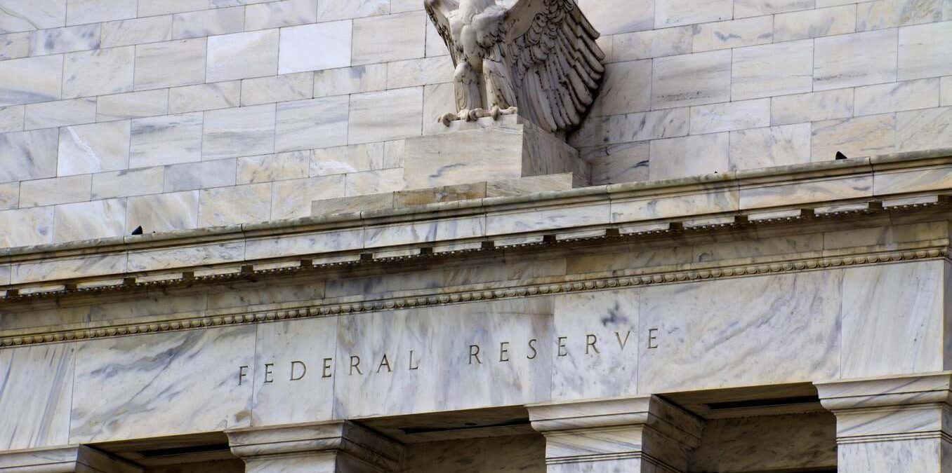 Exterior of the Federal Reserve building showing the word "FEDERAL RESERVE" carved into the marble facade beneath a stone eagle statue