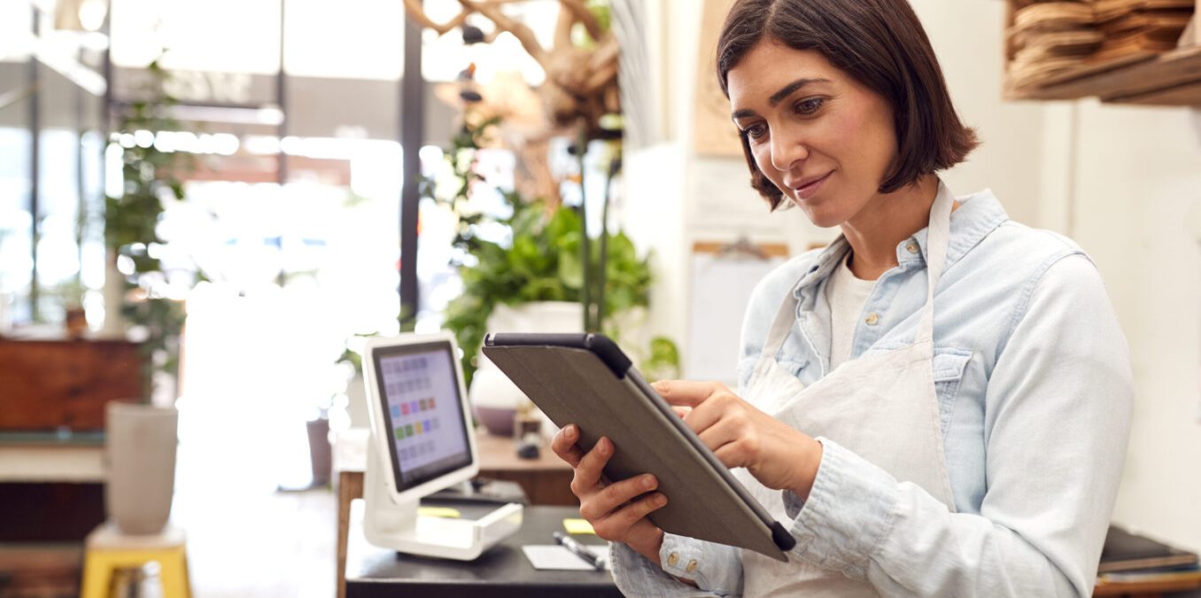 Female owner with digital tablet standing behind sales desk
