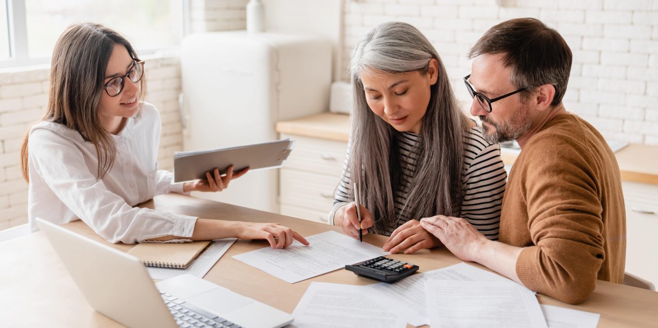 A professional advisor assisting a couple as they sign important paperwork at a desk.