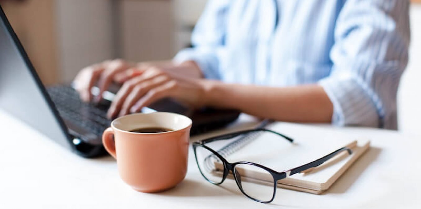 Person works on laptop with a cup of coffee.
